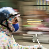Hanoi Street Life 1  The quintessential Vietnamese motorbike girl - and the all are motorbike girls: Hoodie with a girly pattern and mask, more to protect from the sun than from the bad air.